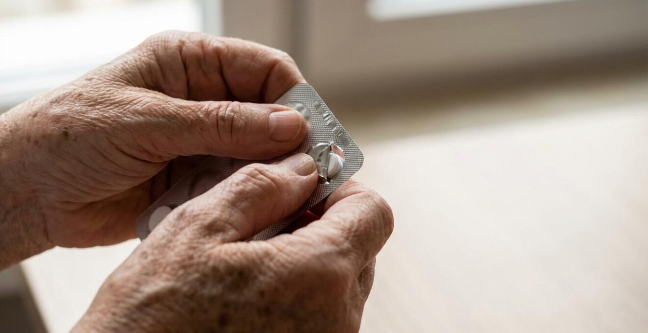 Main de personne âgée manipulant un blister pharmaceutique sécurisé avec témoin d'inviolabilité visible